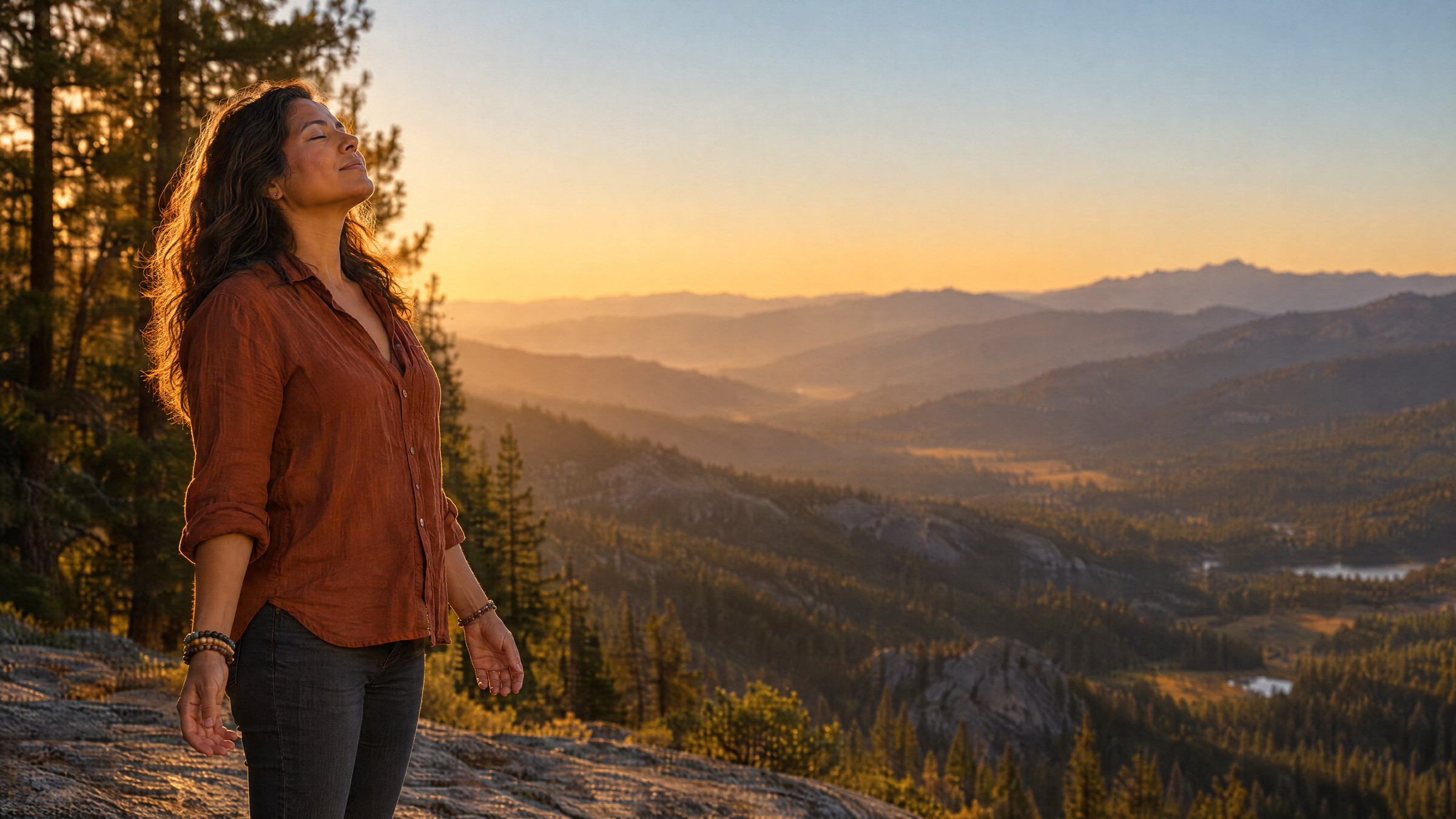 A woman standing at the edge of a Sierra ridge at sunset, eyes closed, face lifted to the light, shoulders released