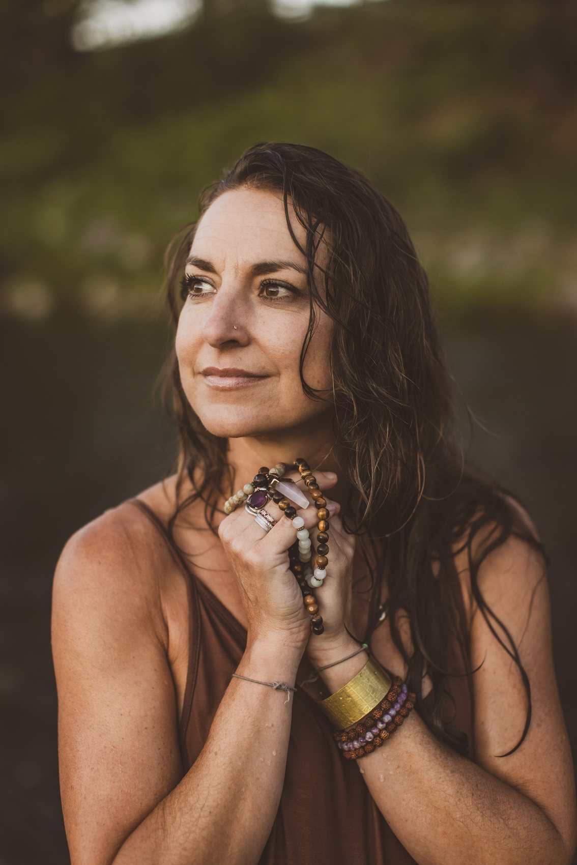 Kaila Leilani by the river at golden hour, holding her mala beads at her heart