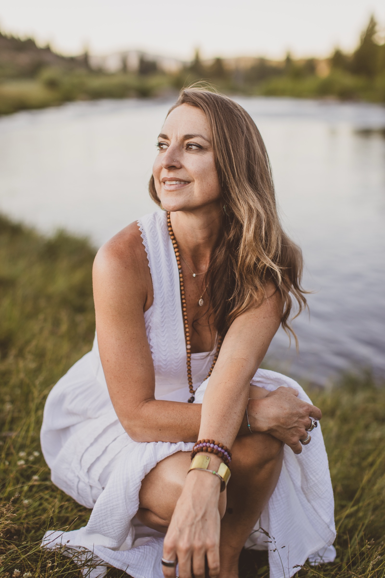 Kaila crouching at the river's edge at golden hour with her hands in the water