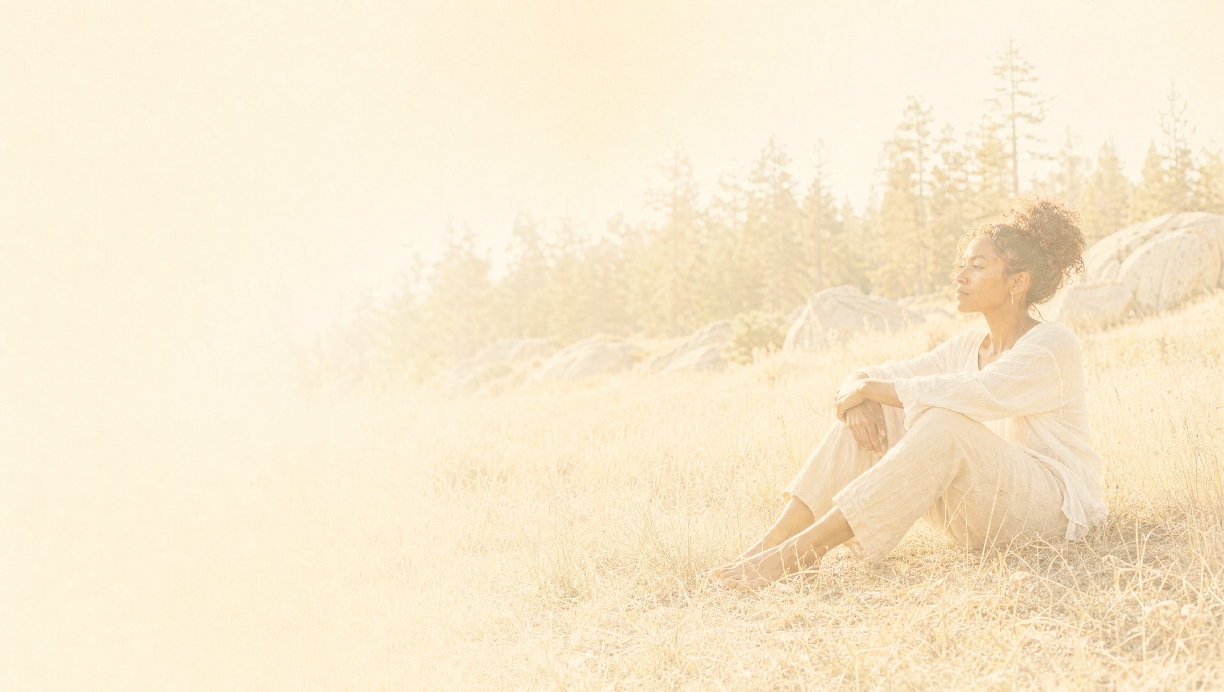A woman sitting alone in a sunlit meadow, the light almost white around her